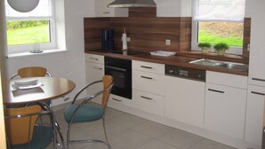 Eine moderne Küche mit weißen Schränken, einer Holzarbeitsplatte, einem eingebauten Backofen und einem Fenster mit Blick auf Grünflächen.