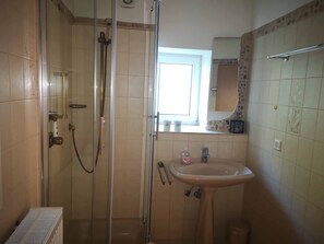 A bathroom with a glass-enclosed shower, a sink, and a window. - Ferienwohnung SOMMER (Winterberg)