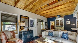A cozy living room with a wooden ceiling, a sofa with blue pillows, a leather chair, and a dark wooden cabinet.
