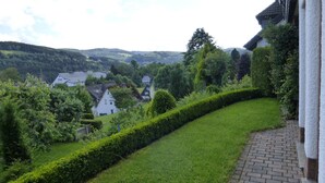 A hillside garden with a curved hedge, a brick pathway, and houses in the background. - Ferienwohnung Dunja (Winterberg)