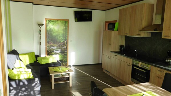 A modern living room with a sofa, a coffee table, and a view of a forest stream through a door.
