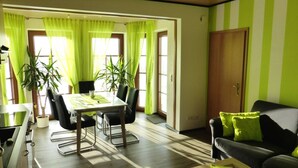 A dining area with a table and chairs, two potted plants, and a sofa with a green pillow. - Ferienwohnung Dunja (Winterberg)