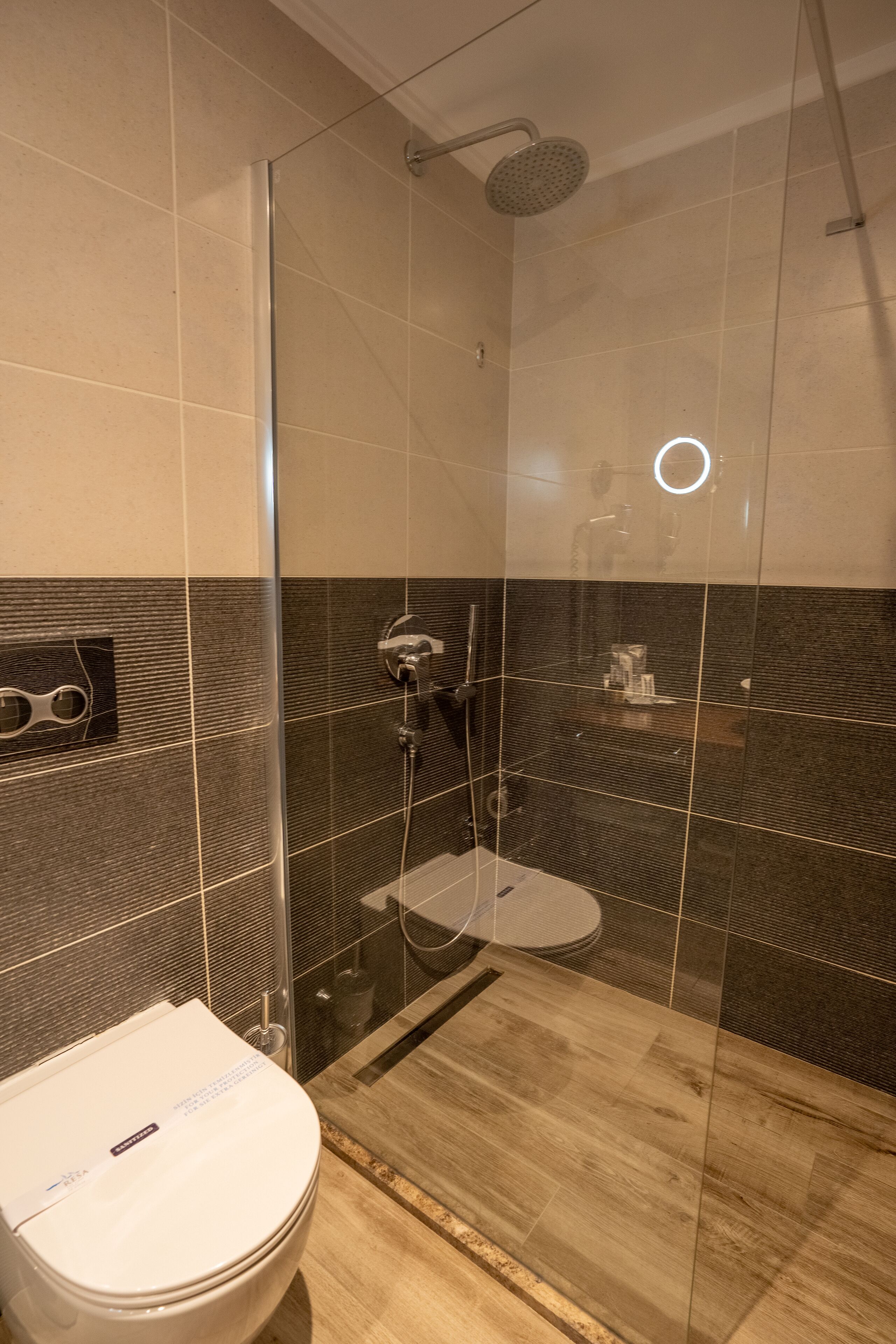 Een moderne badkamer met een douche met glazen wand, een wit toilet en een houten wastafelmeubel.