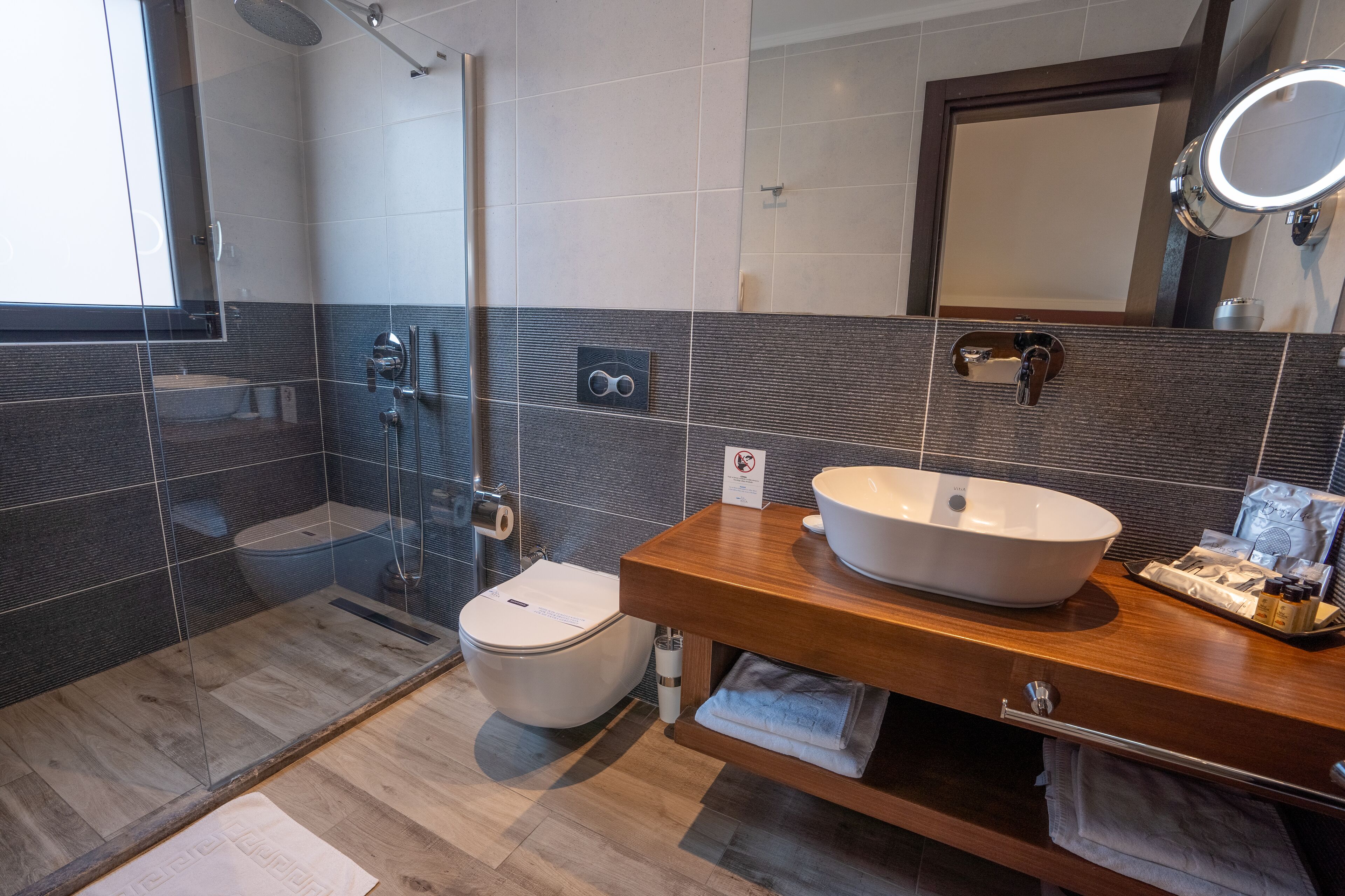 A modern bathroom with a wooden vanity, a large sink, a mirror, and a shower area.
