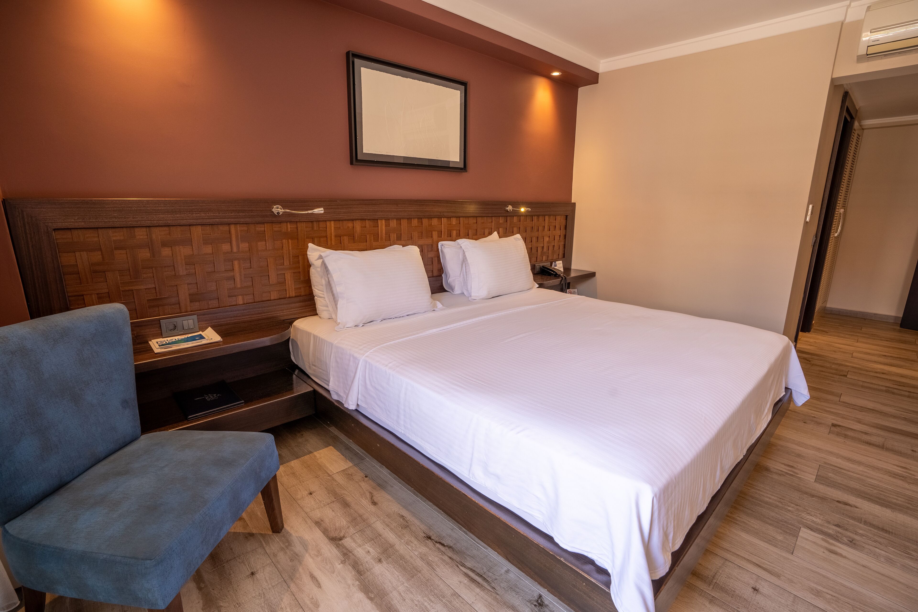 Habitación de hotel con una cama grande, una mesita de noche, una silla y un cuadro en la pared.