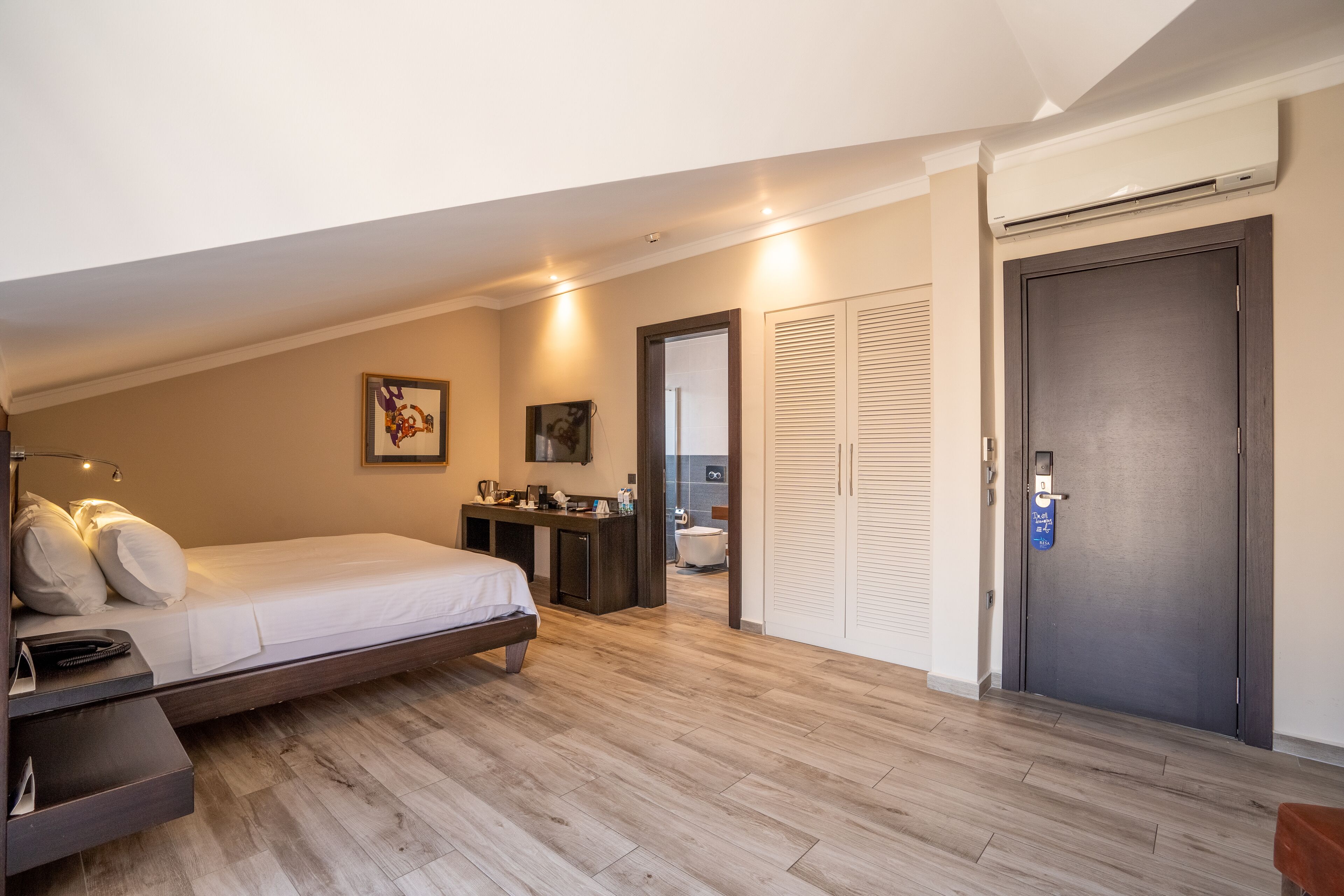 A bedroom with a bed, bedside table, and a desk with a chair. There is a wardrobe and a door with a lock.