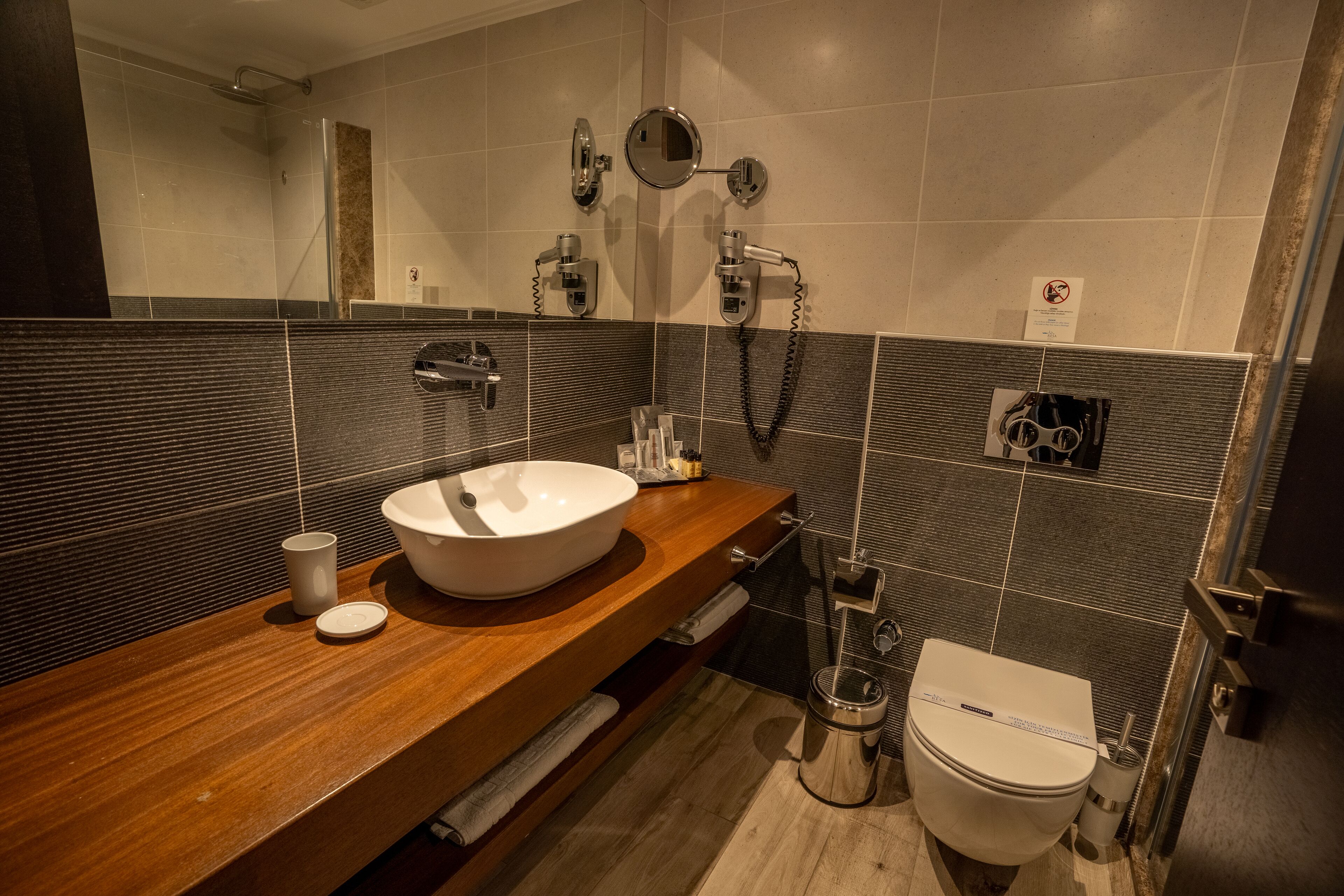 Un baño moderno con tocador de madera, un lavabo grande, un espejo, ducha y retrete.