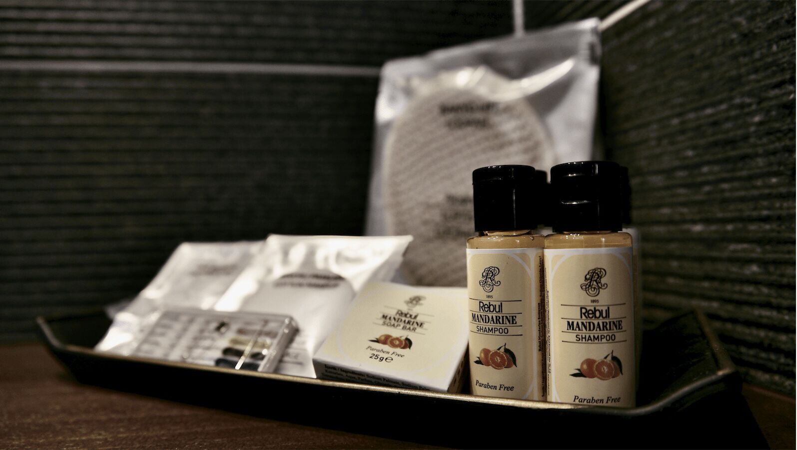 Una bandeja con dos botellas de Champú Mandarina Rebul, una caja de jabón y un pañuelo.