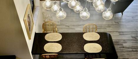 Comedor con una mesa negra, cuatro individuales tejidos, sillas de mimbre e iluminación colgante.