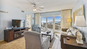 A living room with a TV, sofa, armchair, and a balcony with a view.