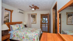 Une chambre à coucher avec un lit en bois, une table de chevet, un ventilateur de plafond et une fenêtre avec un rideau.