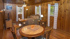 L’intérieur d’un chalet en bois, avec une table à manger ronde, des chaises, un canapé et un ventilateur de plafond.