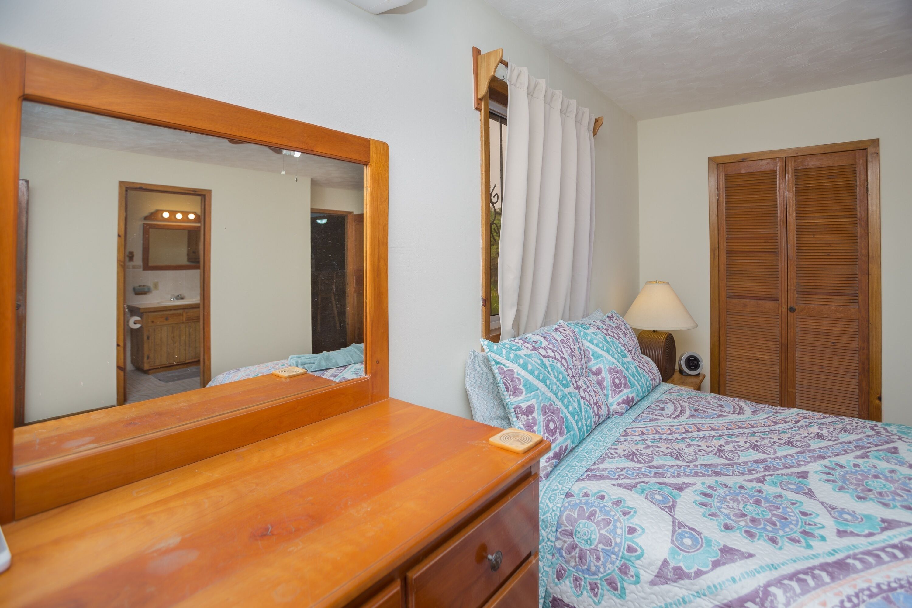 A bedroom with a wooden bed, a large mirror, a bedside table with a lamp, and a wardrobe.