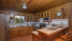 Une cuisine de style rustique, avec des murs en bois, un réfrigérateur, un four à micro-ondes, une cuisinière et des armoires en bois.
