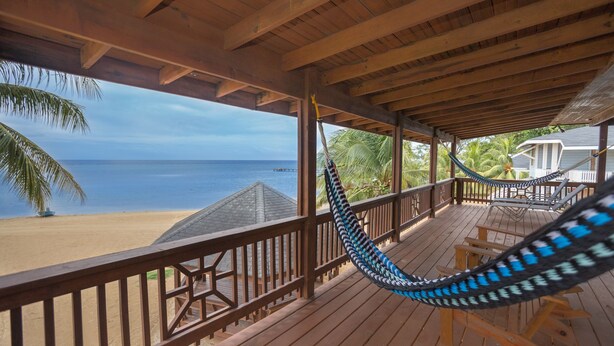 Une terrasse en bois avec un hamac, donnant sur une plage bordée de palmiers et sur l’océan.