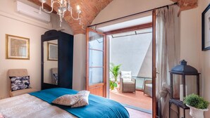 A bedroom with a bed, a chandelier, a door leading to an outdoor area with a chair and plants.