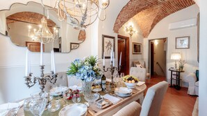 A dining area with a long table set for a meal, featuring a chandelier, candelabras, and a mirror above.