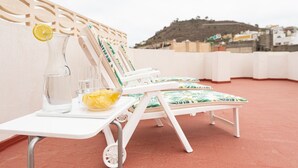 A rooftop terrace with white lounge chairs, a table with a pitcher of water, a bowl of lemons, and a view of a hillside. - HomeForGuest NEW Duplex with Rooftop next to Arucas Cathedral (Arucas)