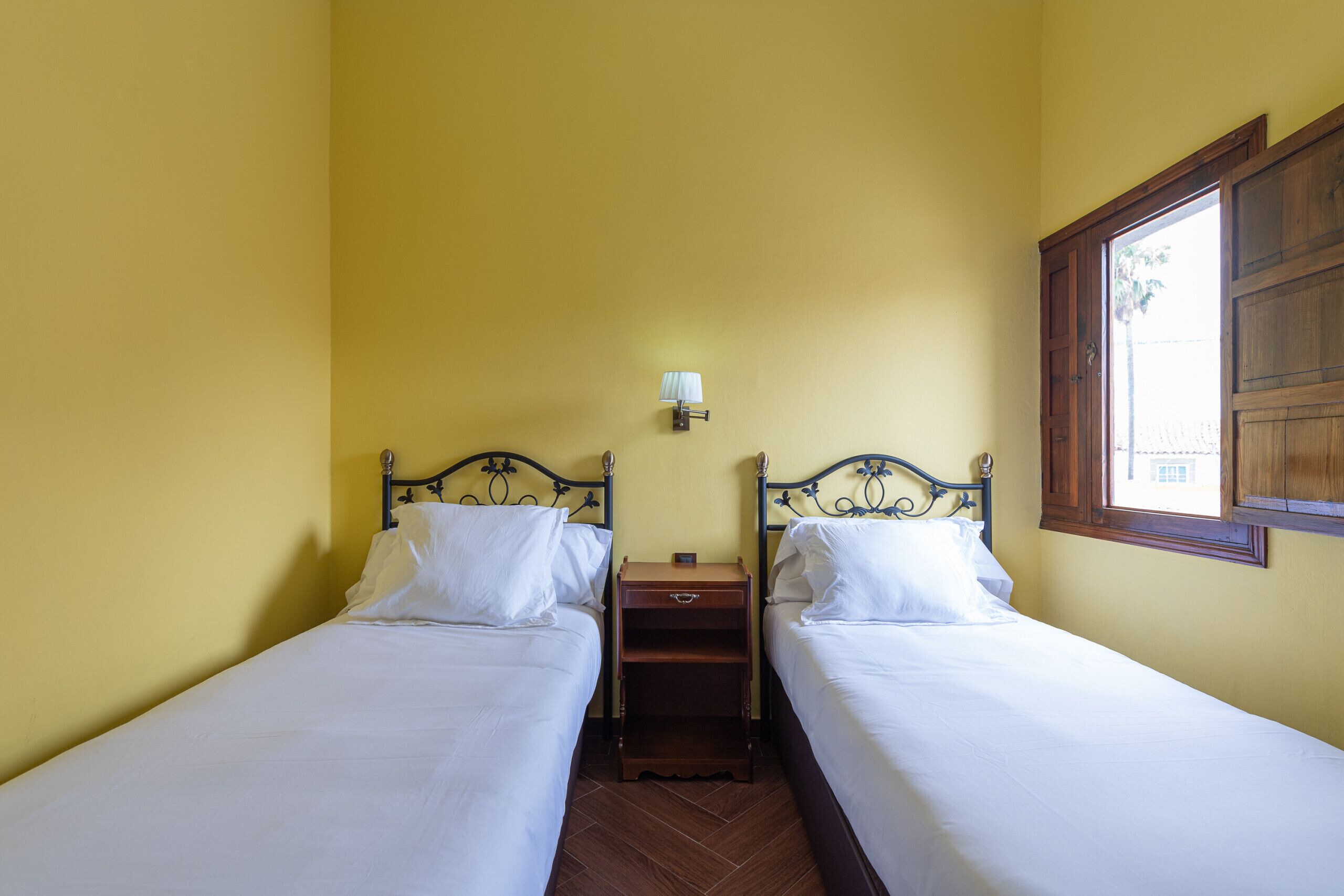 Une chambre avec deux lits simples, une table de chevet placée entre les deux, et une lampe fixée au mur.