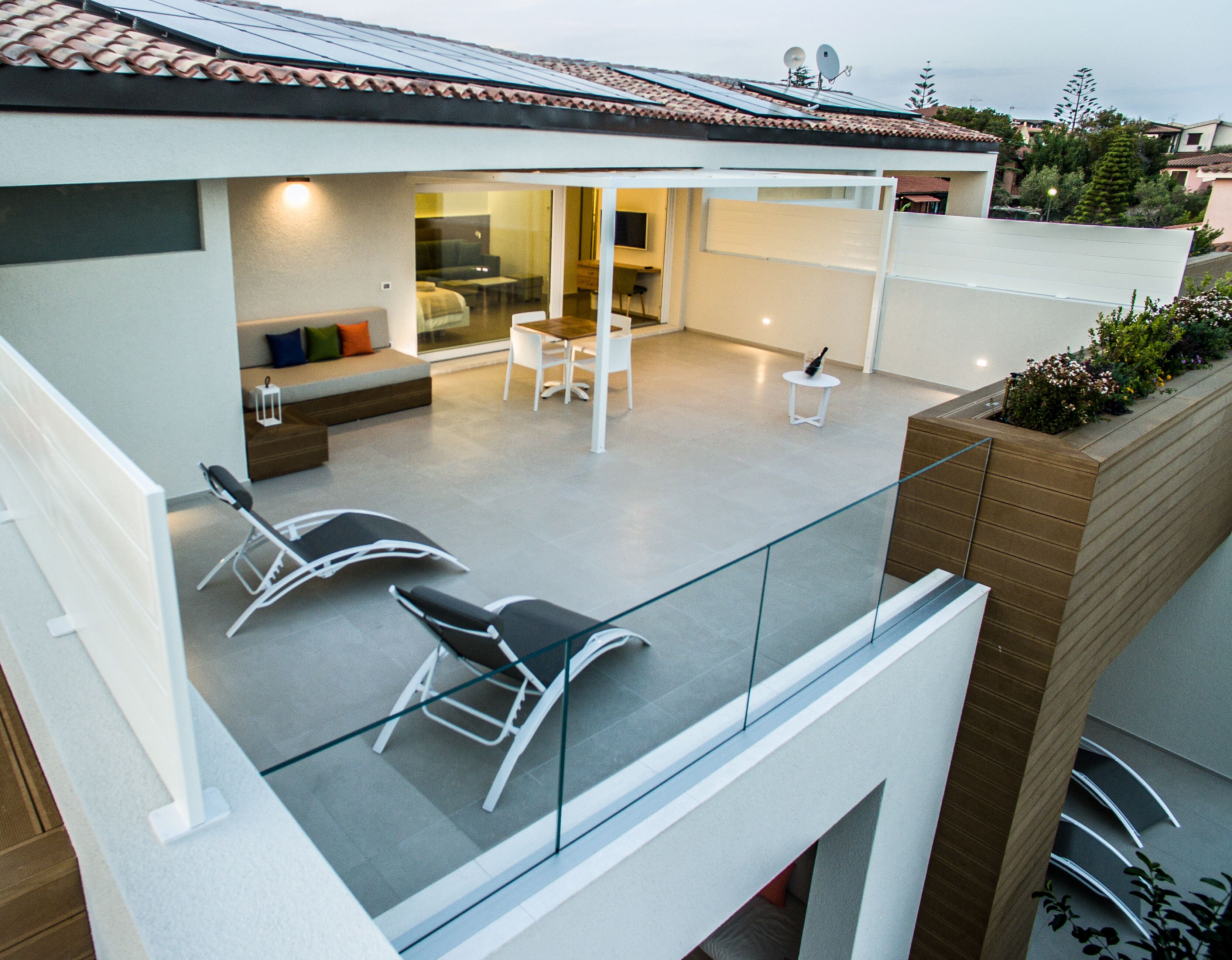 A modern outdoor patio with a glass balustrade, a seating area with a sofa and chairs, and a small table.