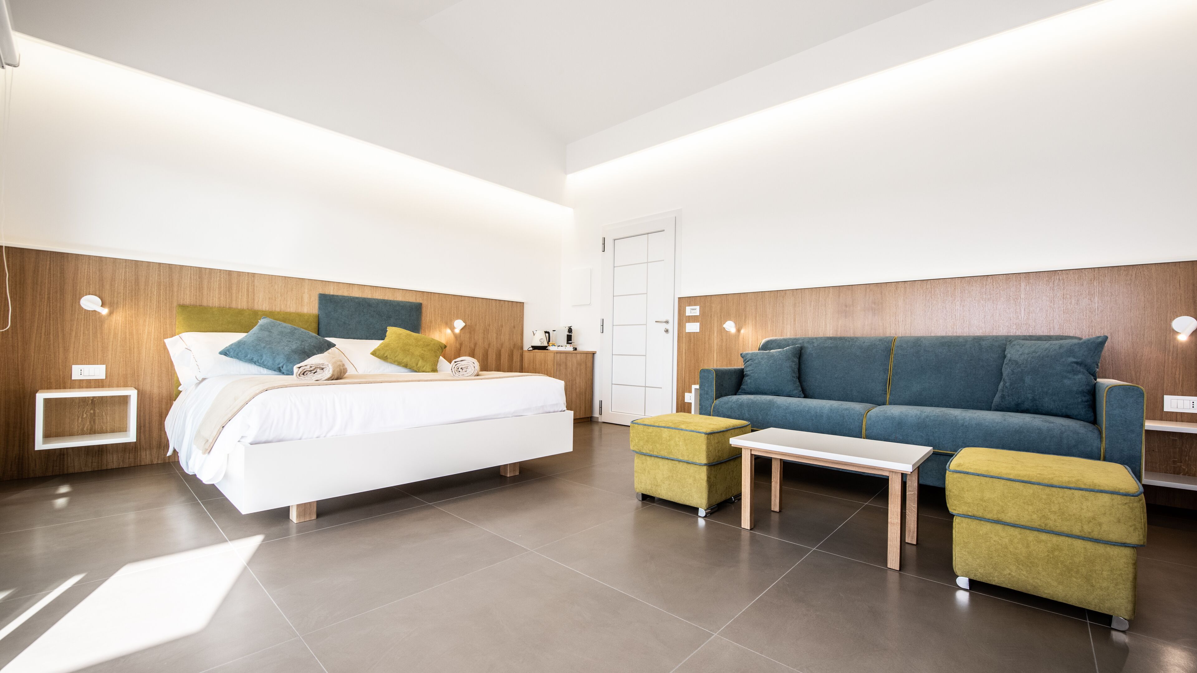 A modern hotel room with a large bed, a blue sofa, and a small table.