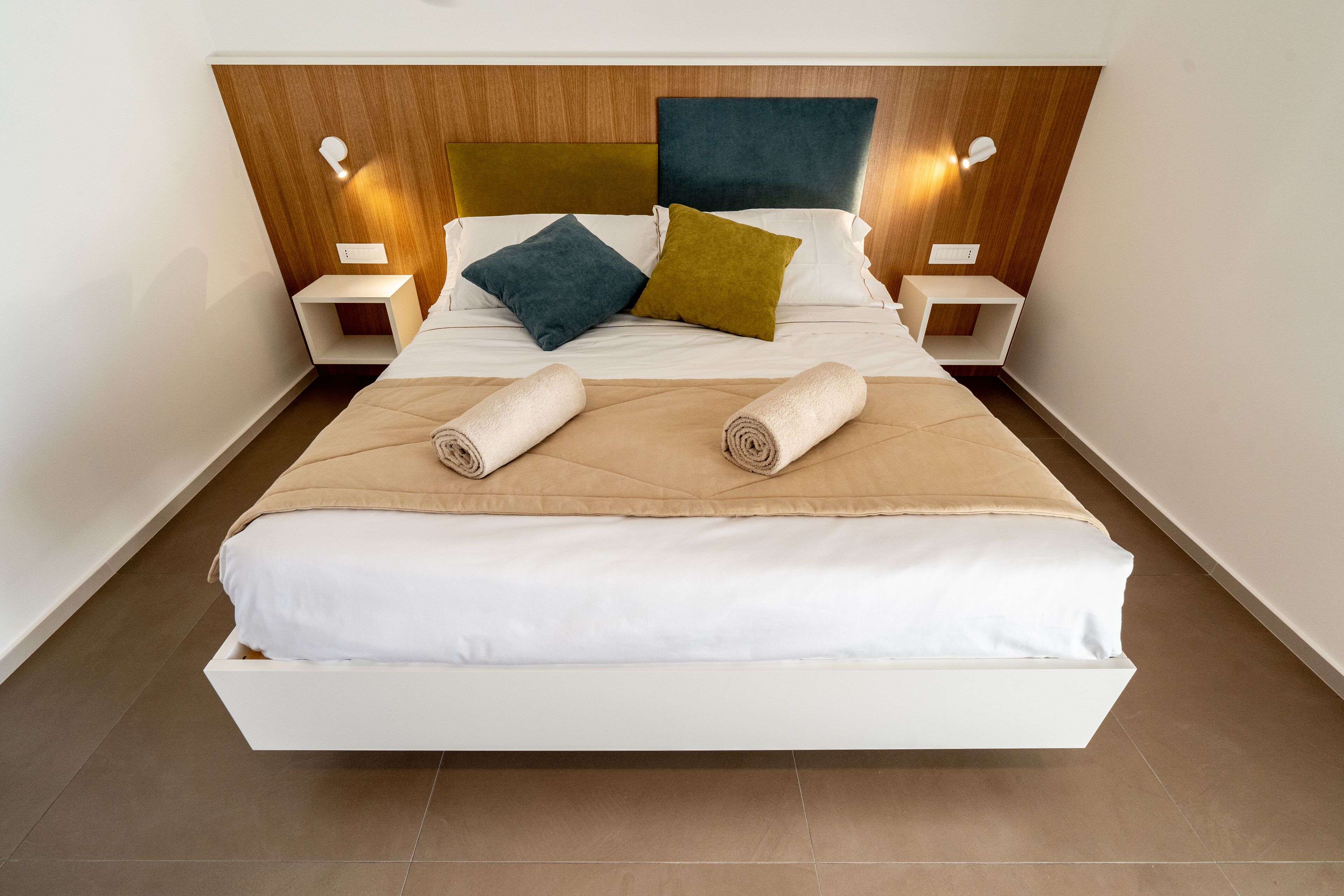 A modern hotel room with a large bed, two bedside tables, and a wooden headboard.