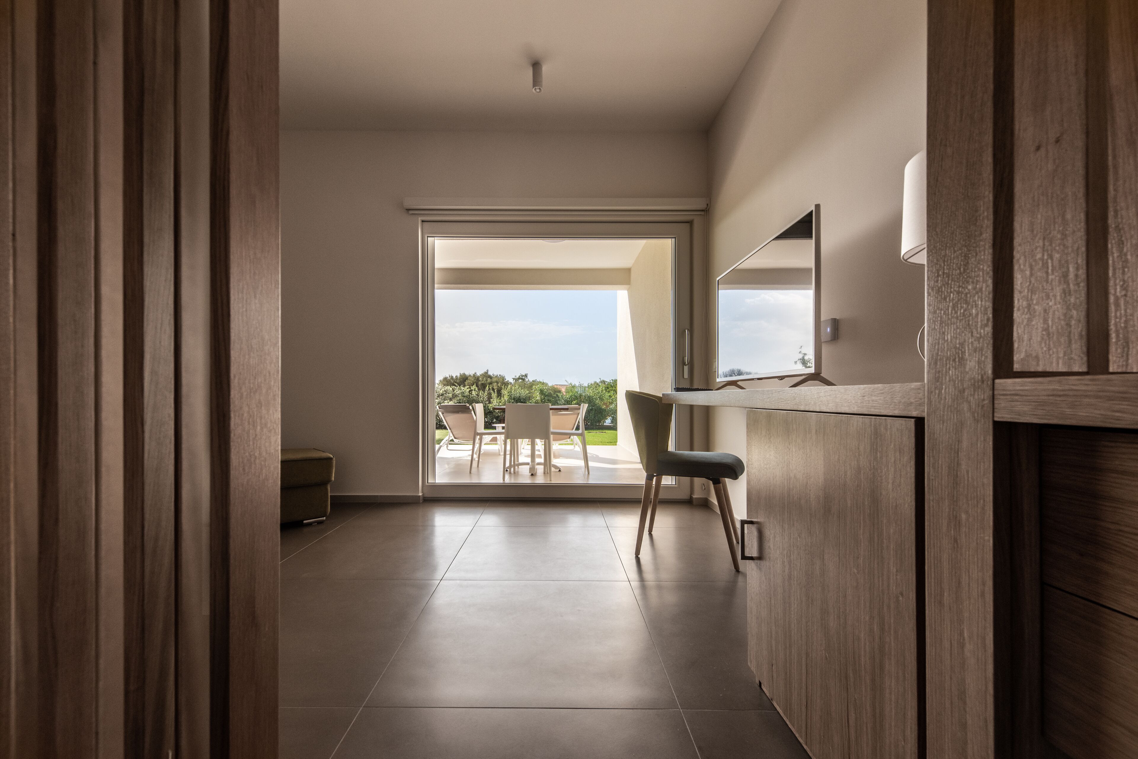 A modern interior with a wooden floor, a desk, and a view of an outdoor patio with chairs and a table.