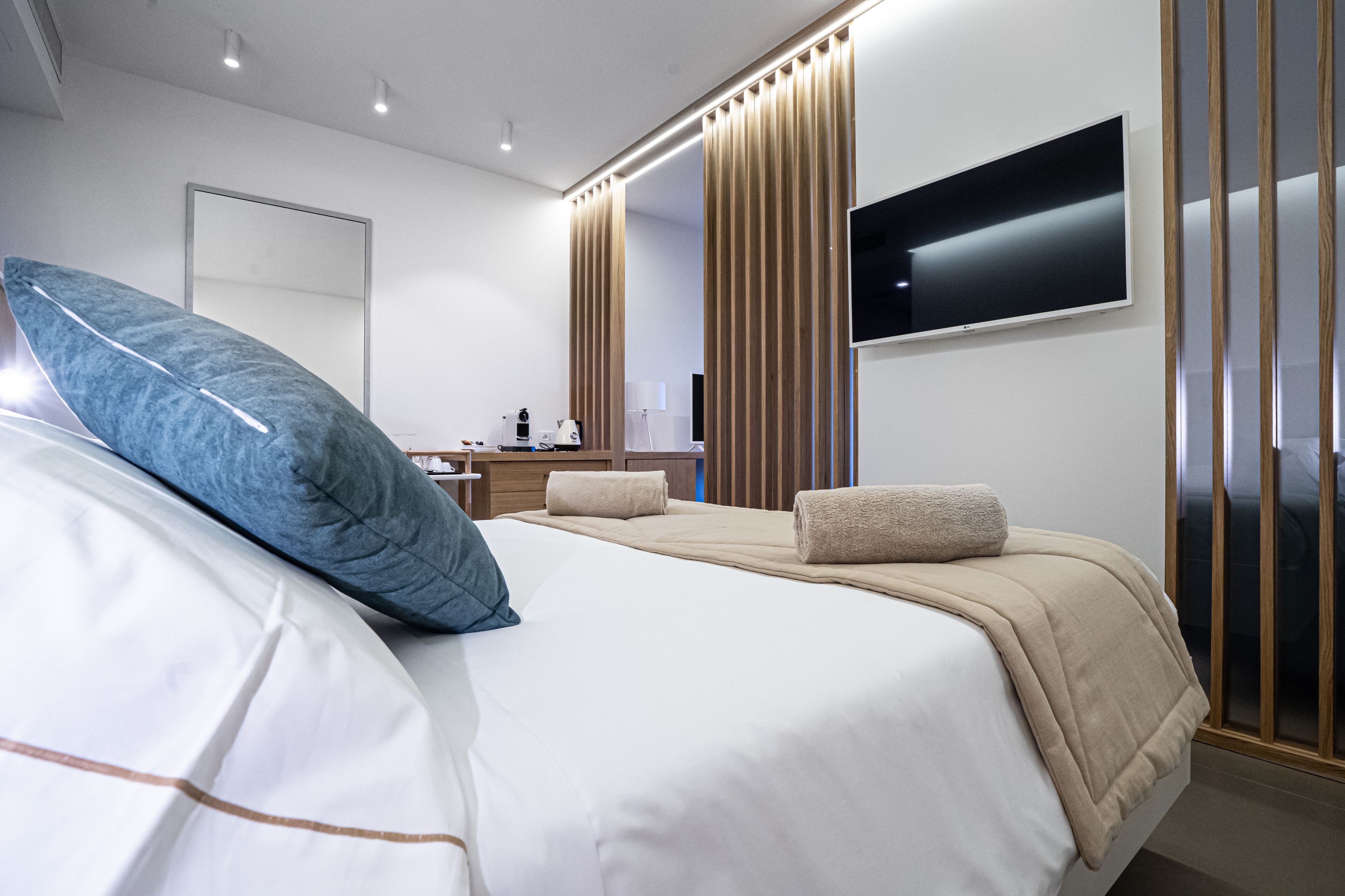 Een moderne hotelkamer met een groot bed, een flatscreen televisie aan de wand en een houten roomdivider.