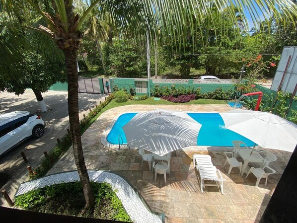 A swimming pool with a sun umbrella, lounge chairs, and a small patio area. - Chalés Praias do Sul (Ipojuca)
