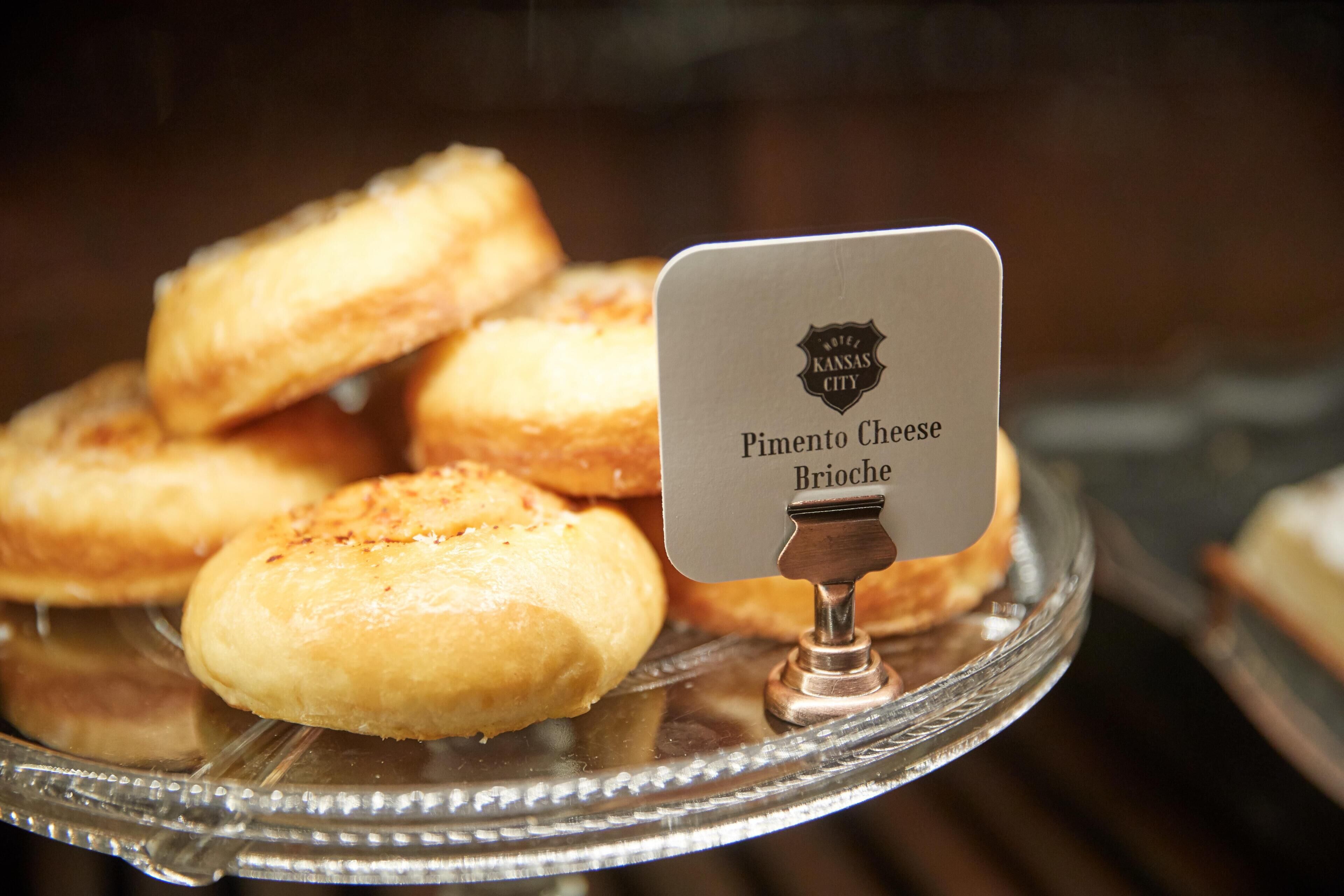 Eine Auswahl an Pimento Cheese Brioche Gebäcken auf einer Glasplatte, mit einem Schild, das den Hotelnamen angibt.