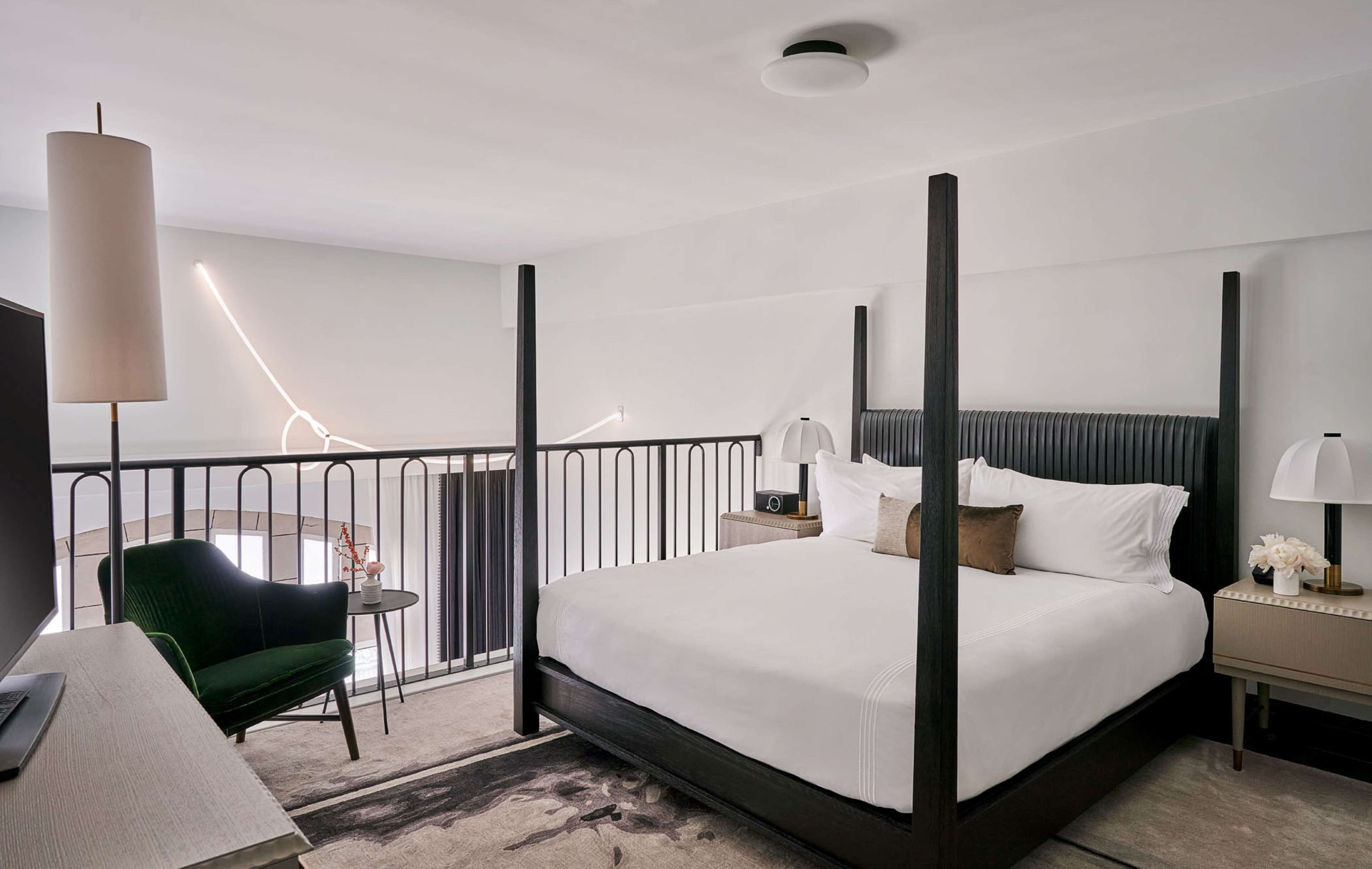 Quarto de hotel moderno com uma cama grande, uma escrivaninha, uma cadeira e uma varanda com guarda-corrimão.
