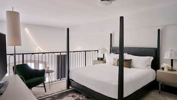 Quarto de hotel moderno com uma cama grande, uma escrivaninha, uma cadeira e uma varanda com guarda-corrimão.