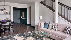 A spacious living area with a high ceiling, a staircase, a dining area, and a sofa with decorative pillows.