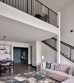 Ein geräumiger Wohnbereich mit hoher Decke, einer Treppe, einem Essbereich und einem Sofa mit Zierkissen.