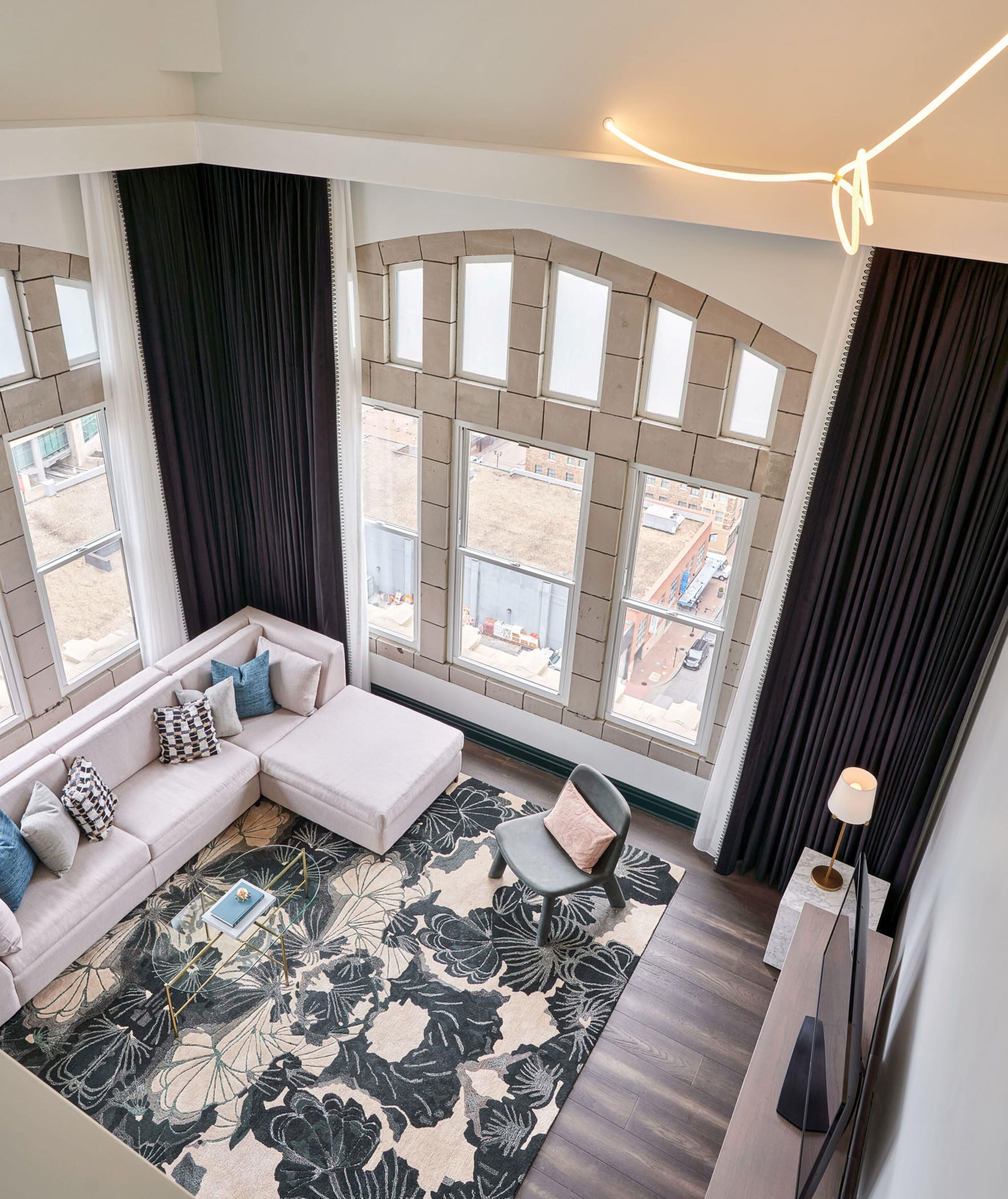 A modern living room with a sectional sofa, a patterned rug, and large windows offering a view of the outside.