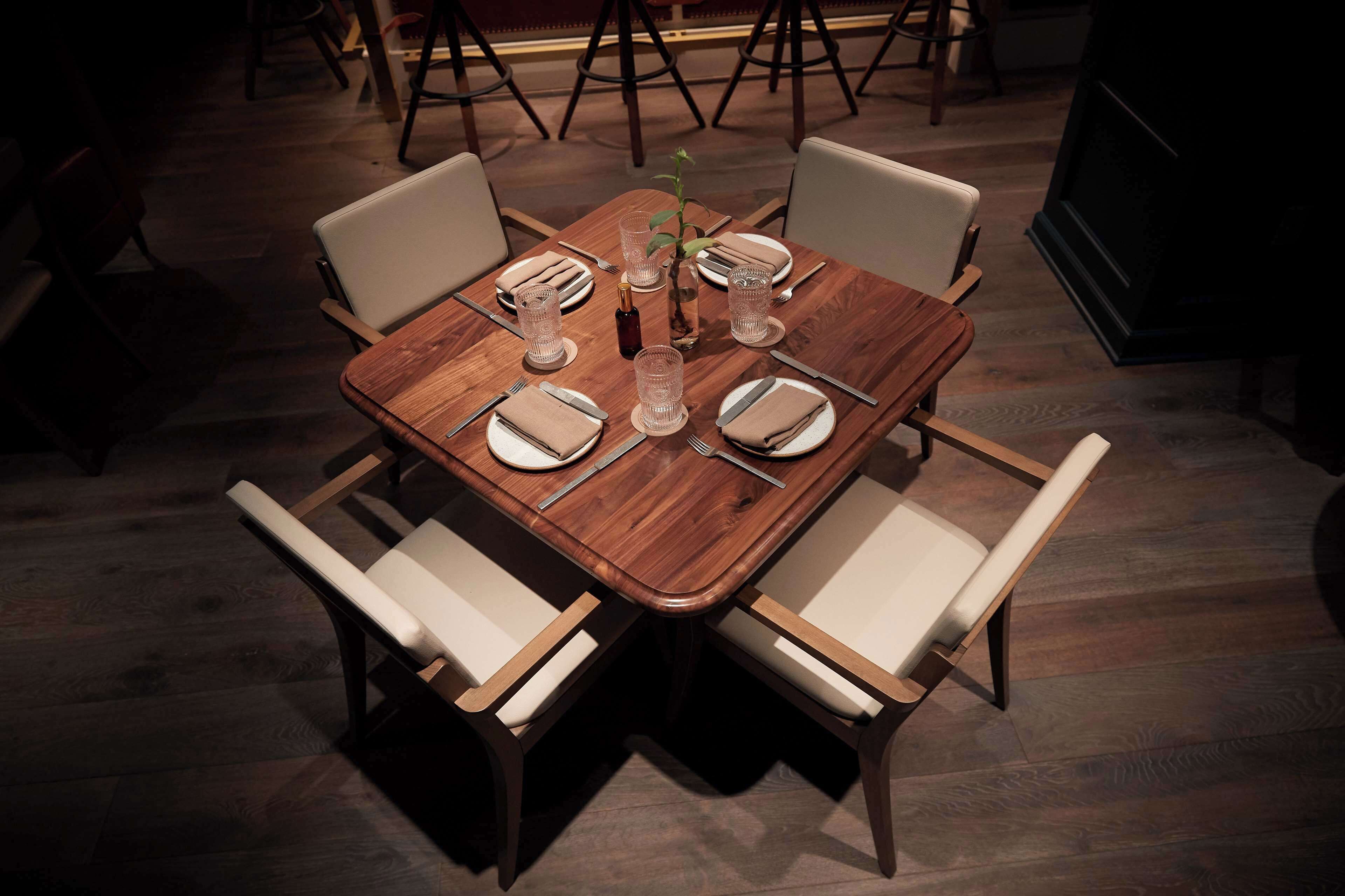 Mesa de comedor preparada para cuatro personas, con sillas blancas, una botella de agua y una pequeña planta.