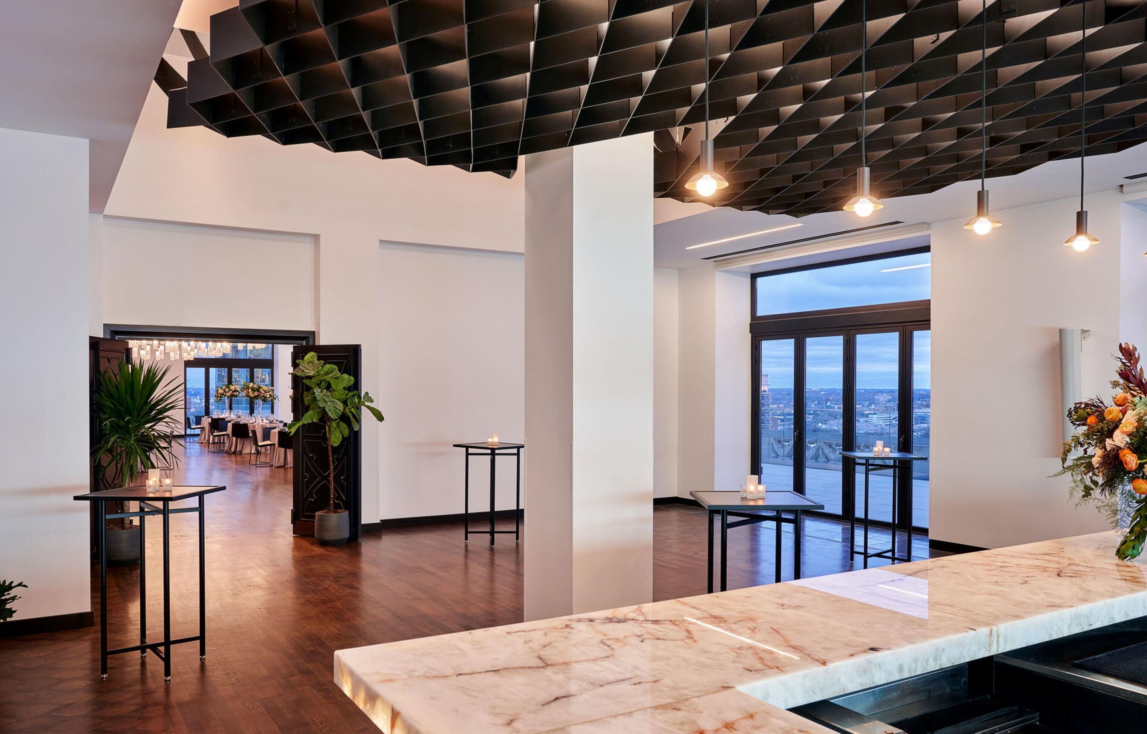 A spacious hotel lobby with a high ceiling, large windows, and a marble reception desk.