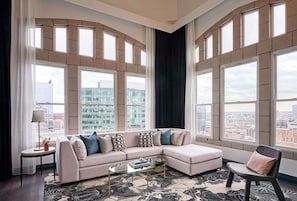 Una sala de estar moderna con un sofá seccional, una mesa de centro de vidrio y ventanas amplias con vistas a la ciudad.