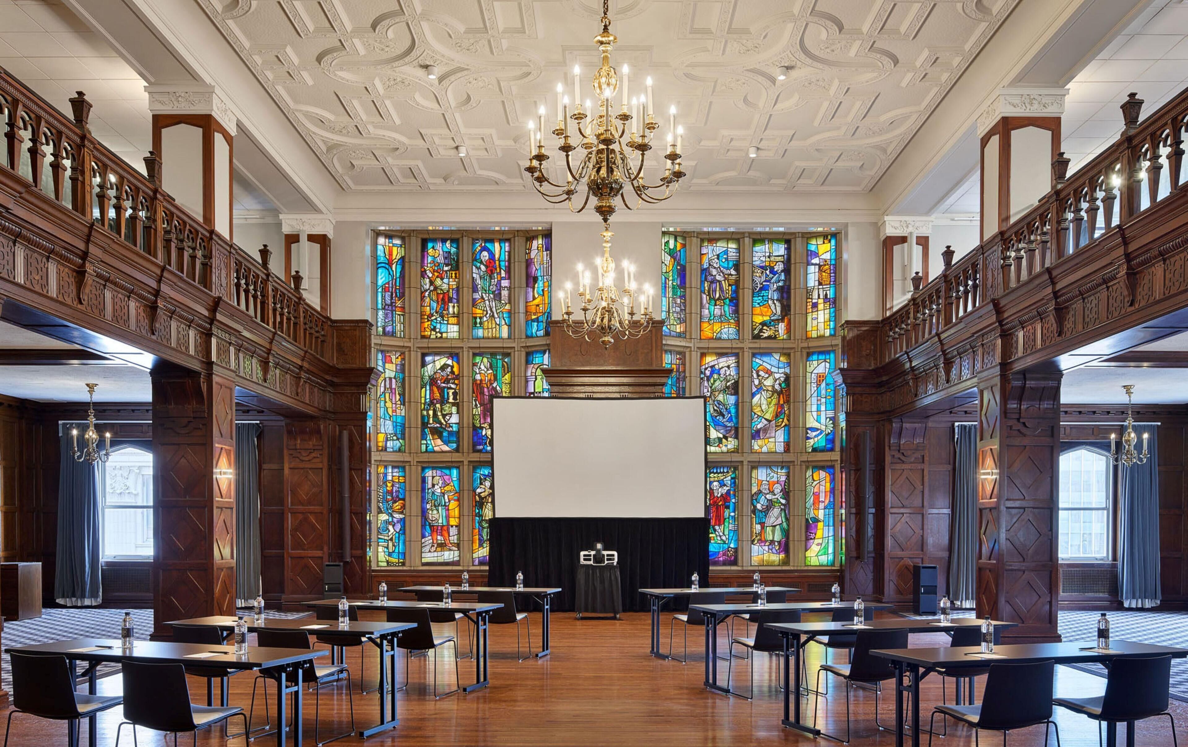 A conference room with a large screen, wooden paneling, and stained glass windows.