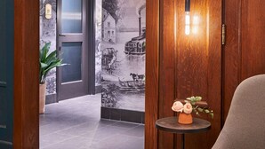 Un vestíbulo de hotel con una puerta de madera, un aplique de pared y una pequeña mesa con un florero.