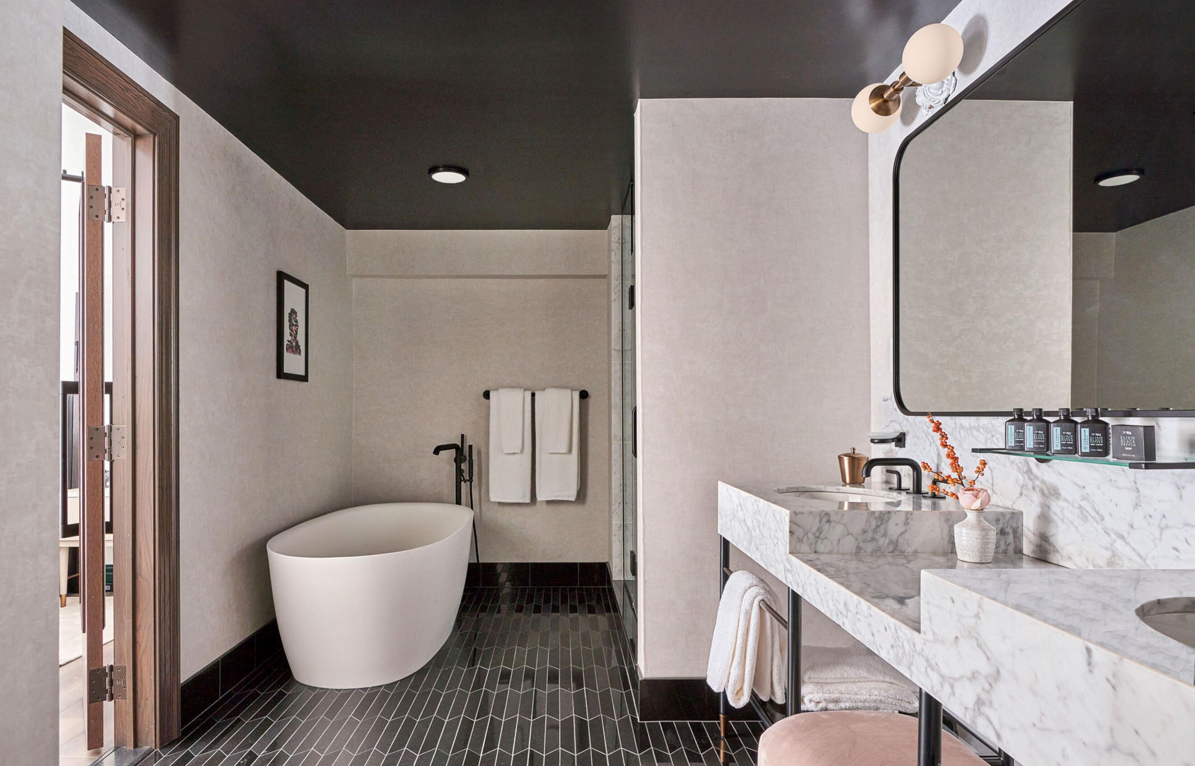 Ein modernes Badezimmer mit einer freistehenden Badewanne, einem großen Spiegel und einer Marmorarbeitsplatte.