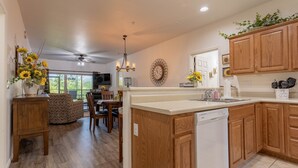 A modern kitchen with wooden cabinets, a dishwasher, and a dining area with a table and chairs. - Vacation, Golf, The Lake, or Shows. Welcome to “Simple Serenity” (Branson West)