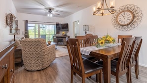 A dining area with a wooden table, chairs, and a chandelier. There is a television in the background and a ceiling fan. - Vacation, Golf, The Lake, or Shows. Welcome to “Simple Serenity” (Branson West)