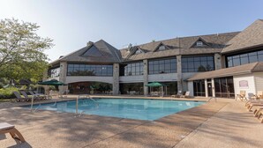 A pool area with lounge chairs and umbrellas, a building with large windows and stone pillars, and a clear sky. - Vacation, Golf, The Lake, or Shows. Welcome to “Simple Serenity” (Branson West)