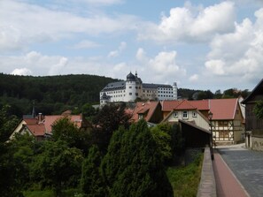 A castle-like building with a red-tiled roof, surrounded by residential buildings and greenery. - Large vacation apartment with 180-degree views of the mountains (Sankt Andreasberg)