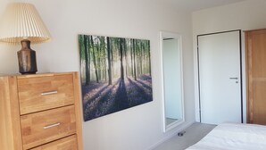 Un dormitorio con un aparador de madera, un espejo y un cuadro de un sendero en el bosque.