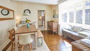A cozy living room with a wooden dining table, white chairs, a sofa, and a window with a view of the outside. - Host & Stay | Princes Road (Saltburn-by-the-Sea)