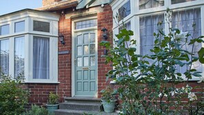 A traditional brick house with a green door, white-framed windows, and a small porch with potted plants. - Host & Stay | Princes Road (Saltburn-by-the-Sea)