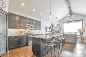A modern kitchen with dark cabinets, a large island with bar stools, and a ceiling fan.