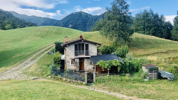 Une maison de campagne à l’aspect rustique, avec une façade en pierre, un balcon en bois et un petit jardin.